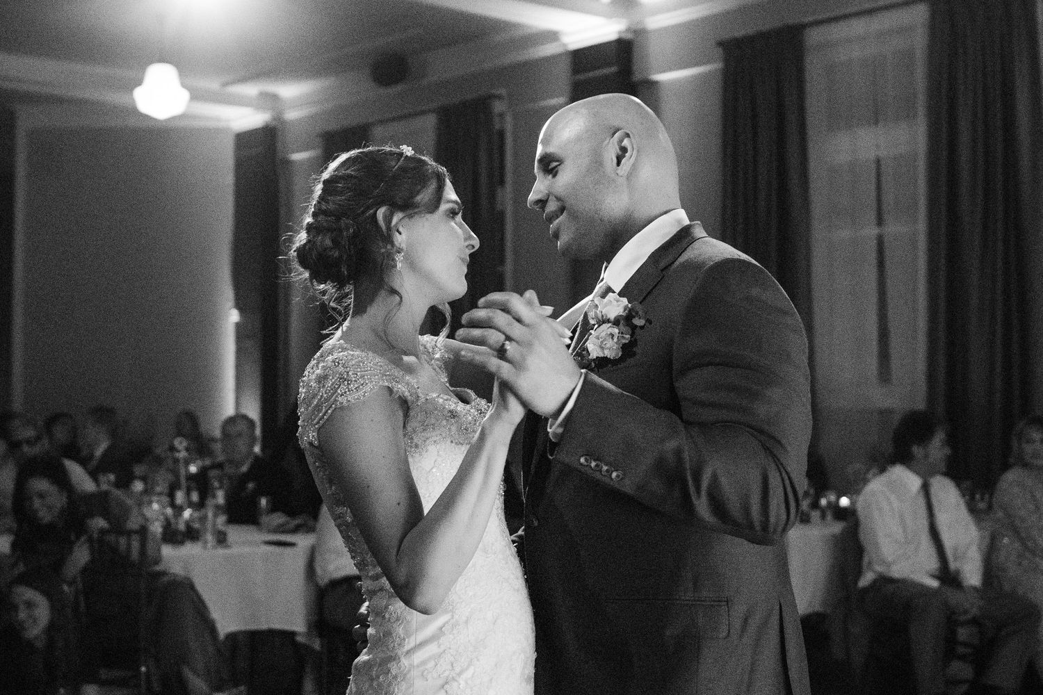 A black and white photo of a couple sharing their first dance at a wedding reception.