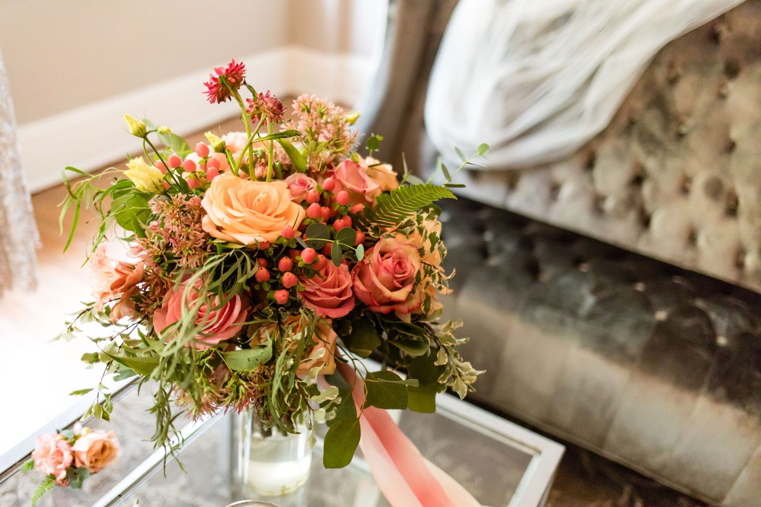 A beautiful floral arrangement with coral roses and greenery on a glass table.