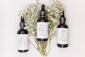 Three black dropper bottles with white labels arranged with delicate baby's breath flowers on a light background.