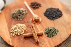 Various dried spices and herbs arranged on a wooden cutting board with cinnamon sticks and a honey dipper.