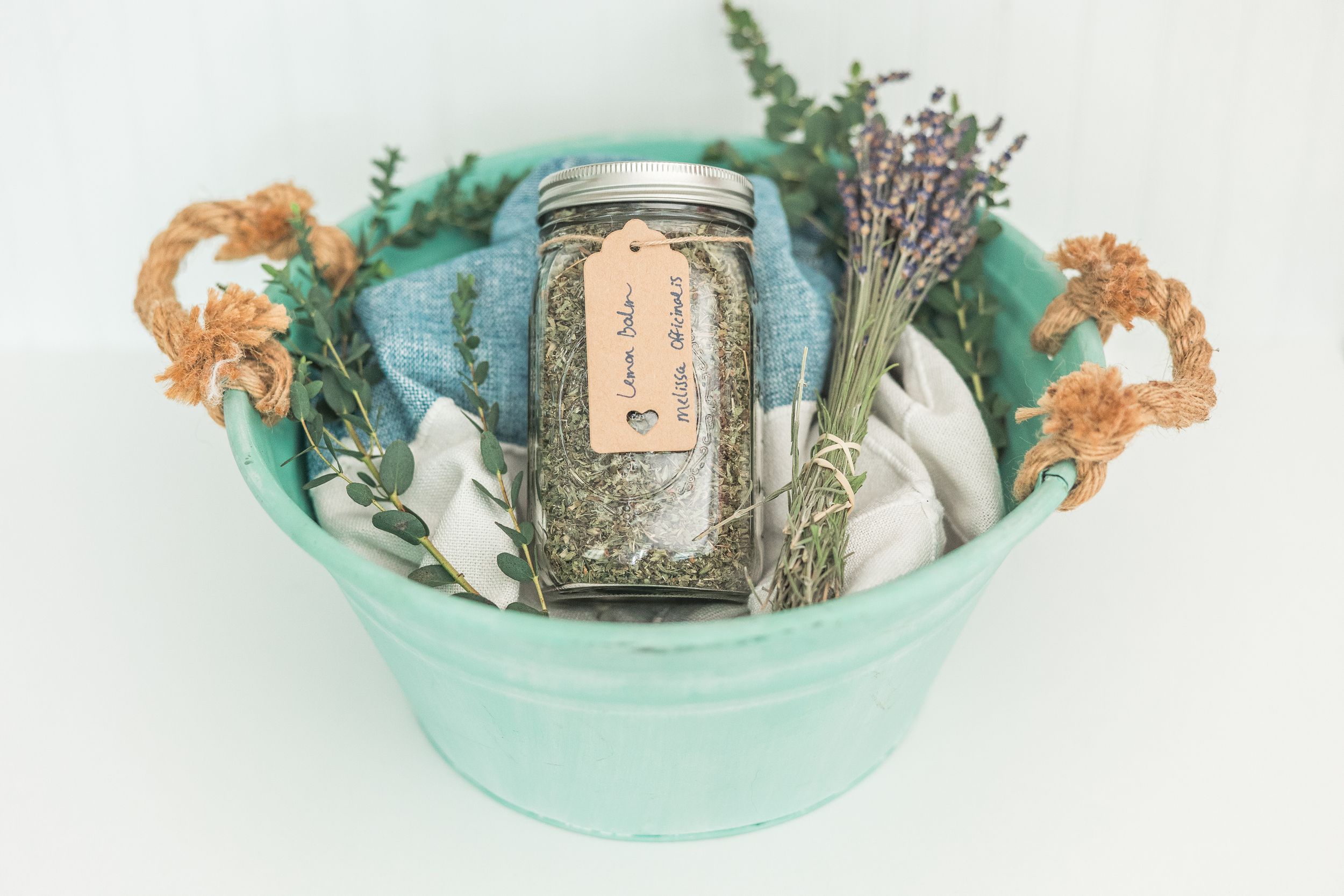 A mint green ceramic bowl contains dried flowers and herbs with a vintage glass jar in the center.
