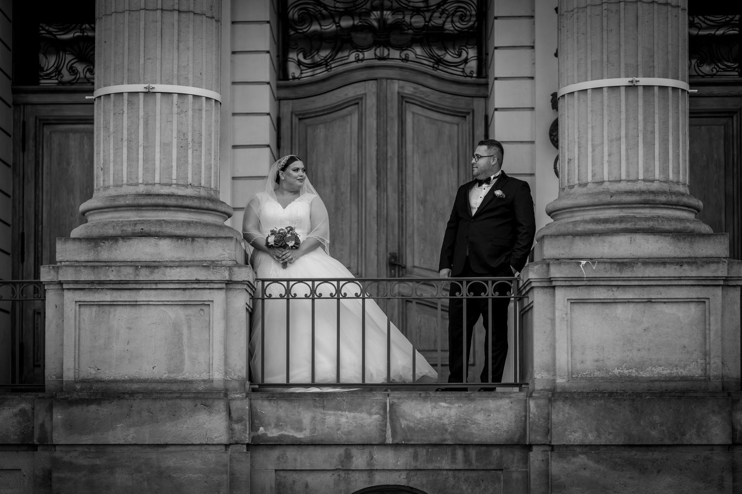 Schwarz-Weiß-Fotografie eines Brautpaares in Berlin Mitte, das zwischen klassischen Steinsäulen steht – zeitlose und elegante