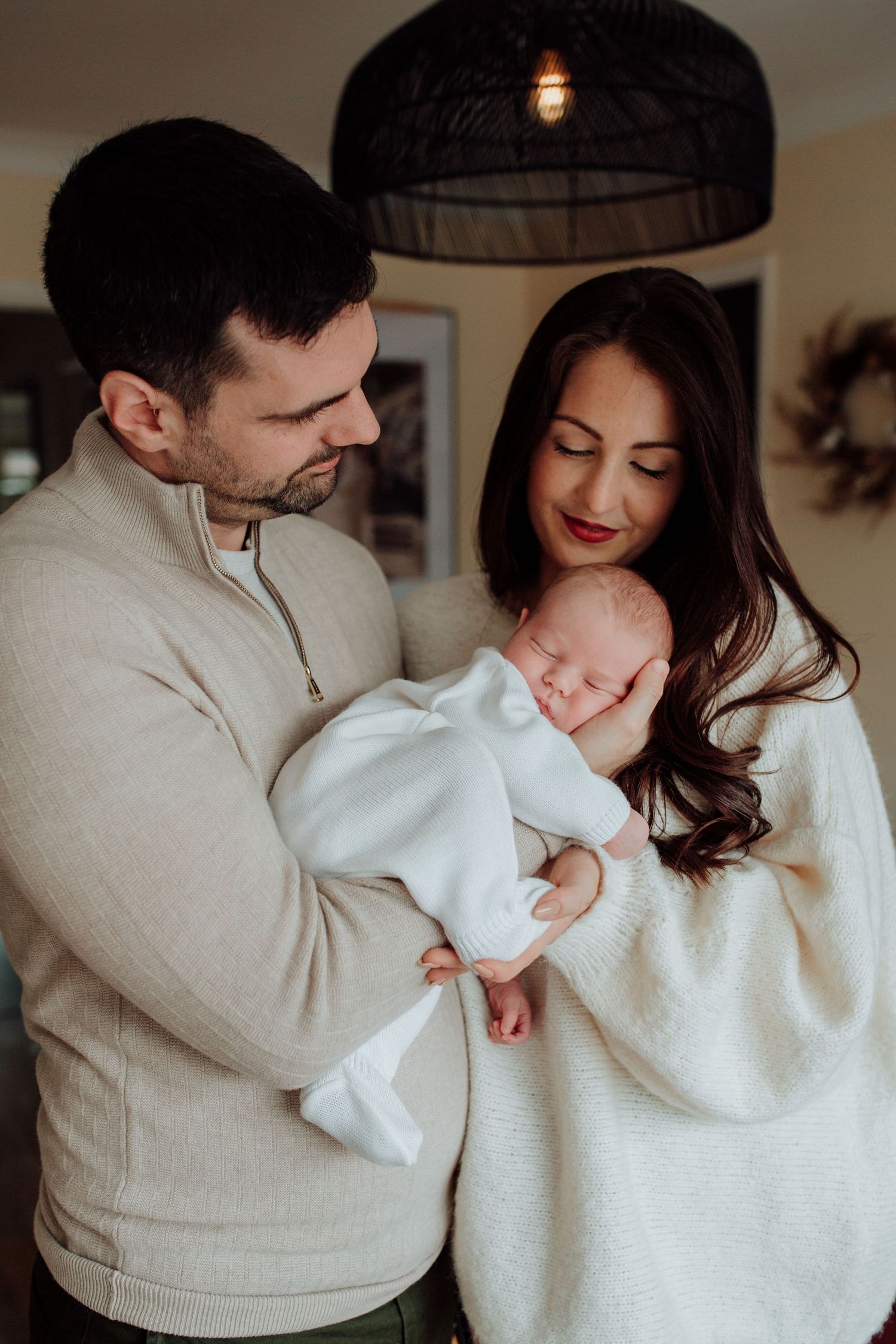A tender moment of parents cradling their sleeping newborn baby while standing in their cozy home.