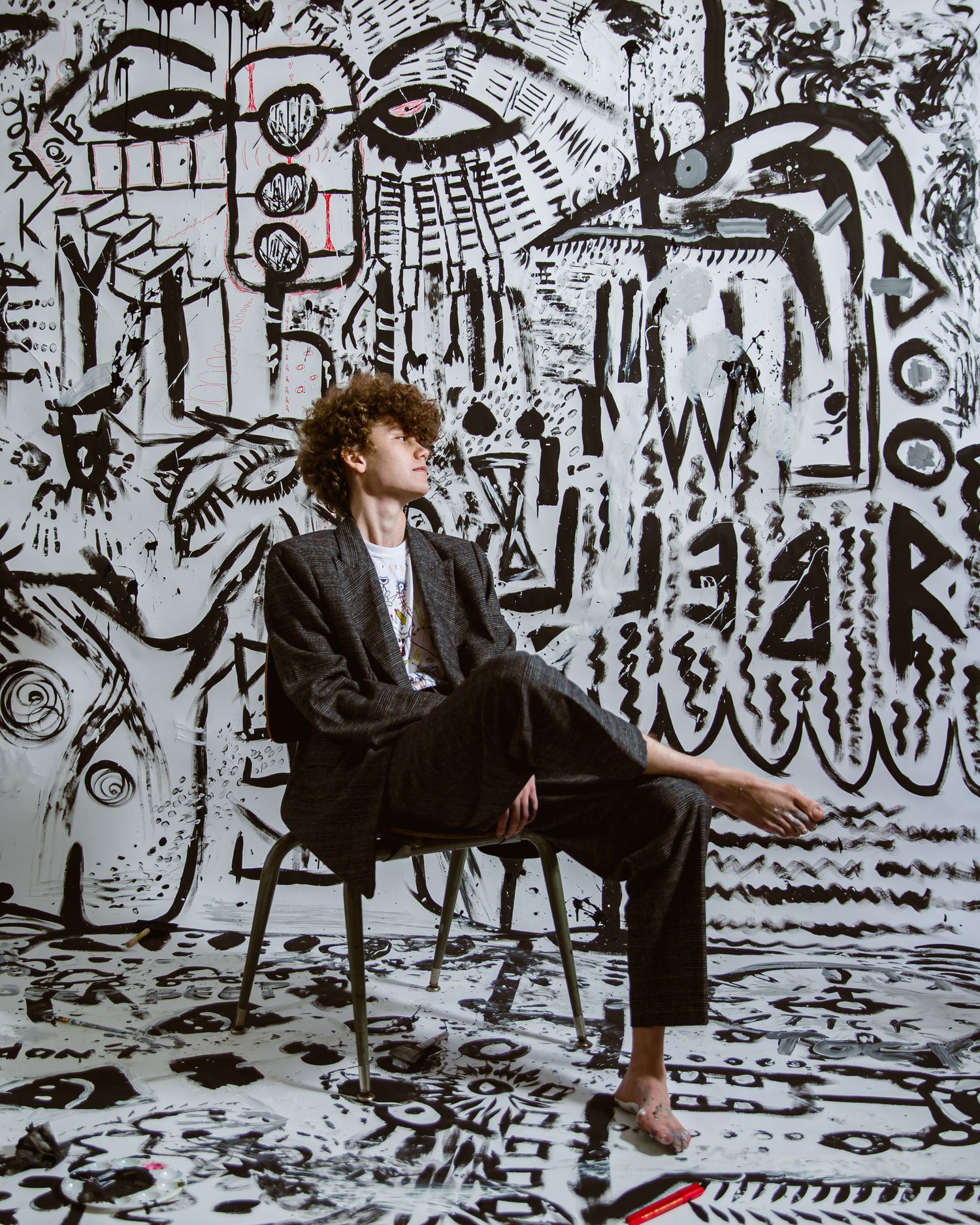 Person seated in front of black and white artistic graffiti wall with intricate doodle designs and patterns.