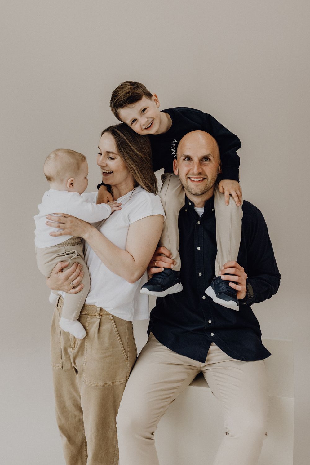 Studioshooting einer Familie im Fotostudio. Der Sohn ist auf der Schulter des Vaters, die Mutter hält ein Kind auf dem Arm.