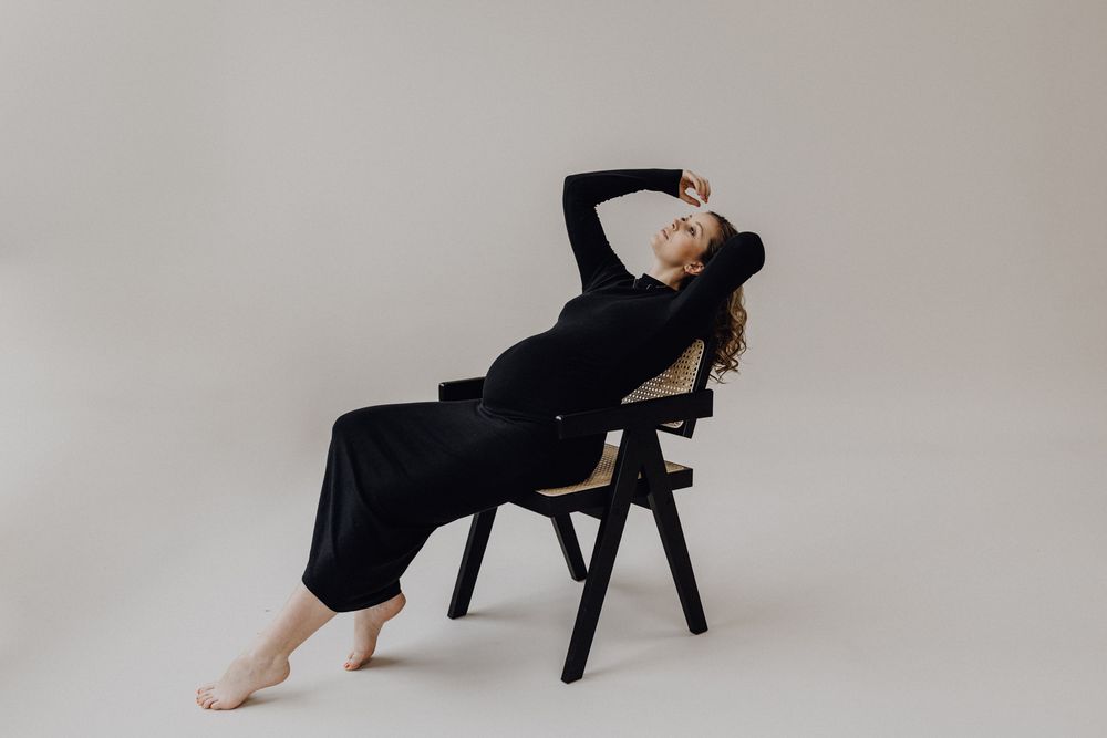 Studiosession in Heidelberg mit einer Schwangeren. Die Schwangere trägt ein enges schwarzes Kleid und sitzt auf einem schwarzen Stuhl.