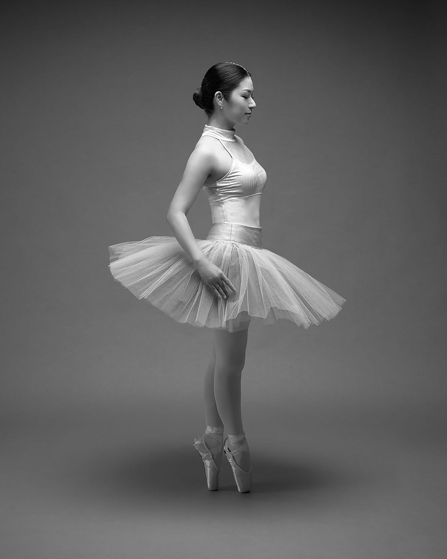 A ballet dancer in a white tutu performs graceful movements in a dramatic black and white studio portrait series.