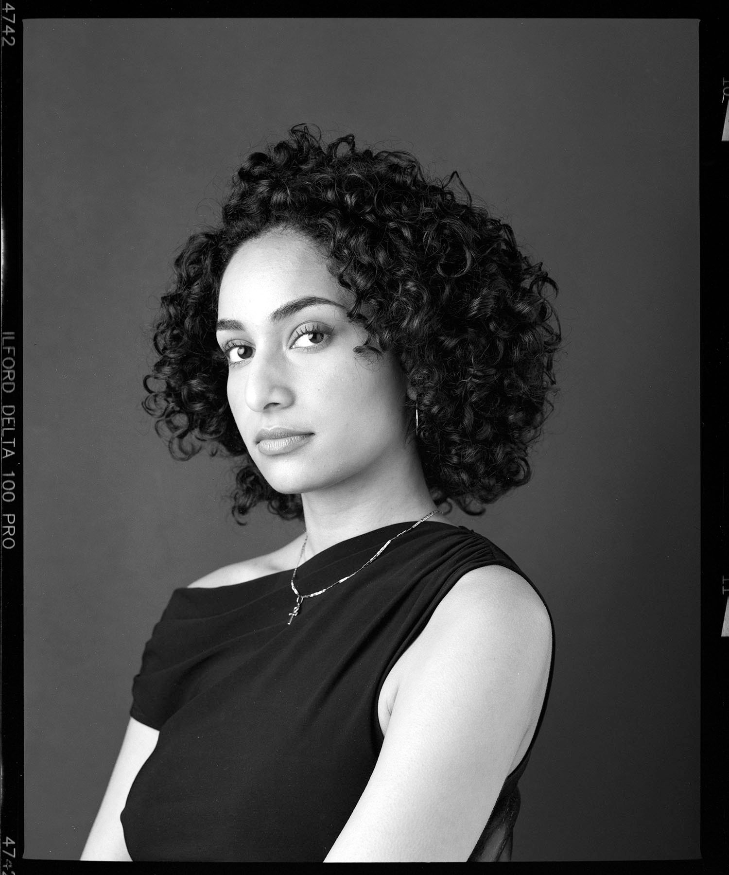 A series of black and white studio portraits showing different angles of a person with curly hair in a sleeveless black top.