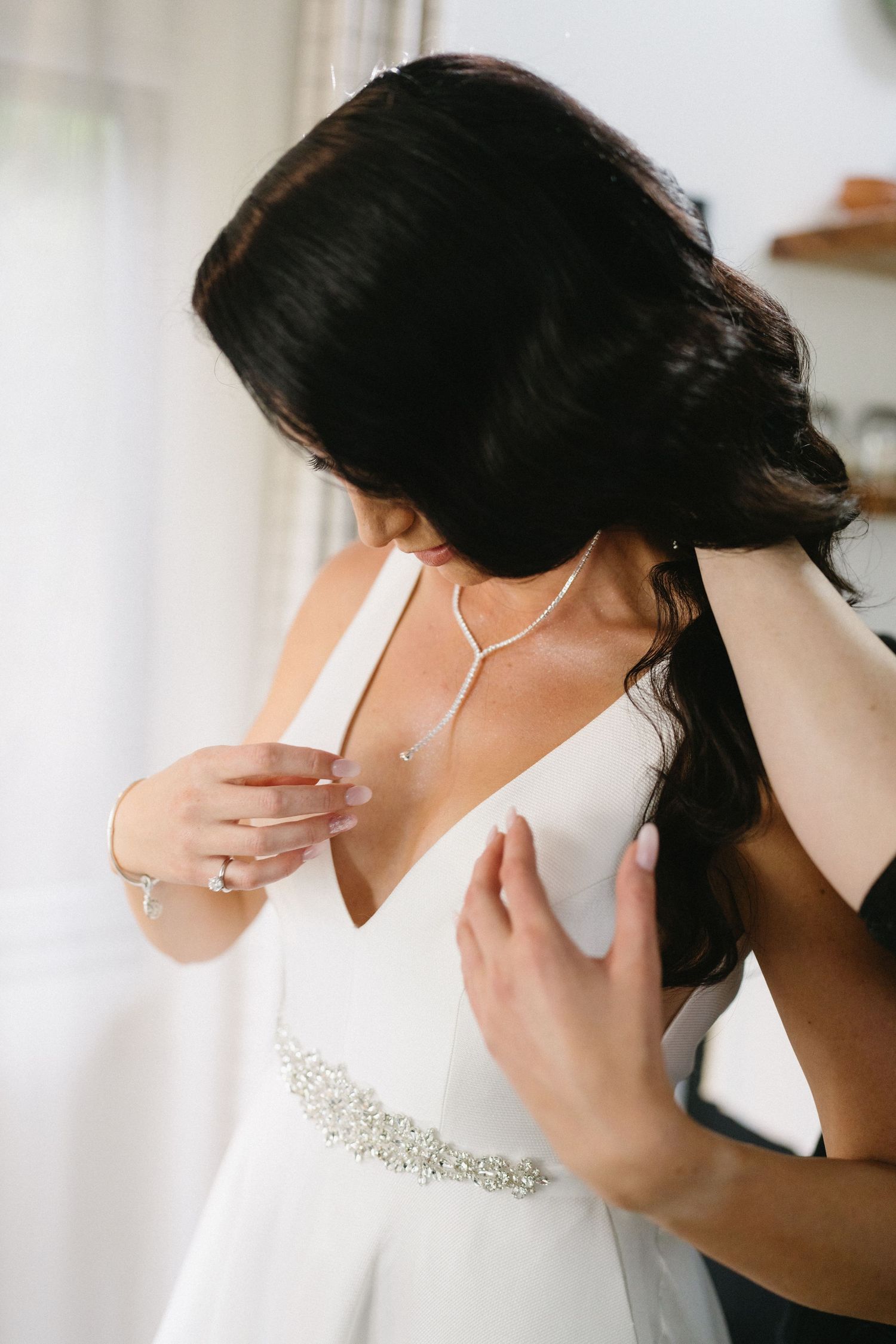 Detail shot of bride adjusting wedding dress with crystal belt and delicate necklace.