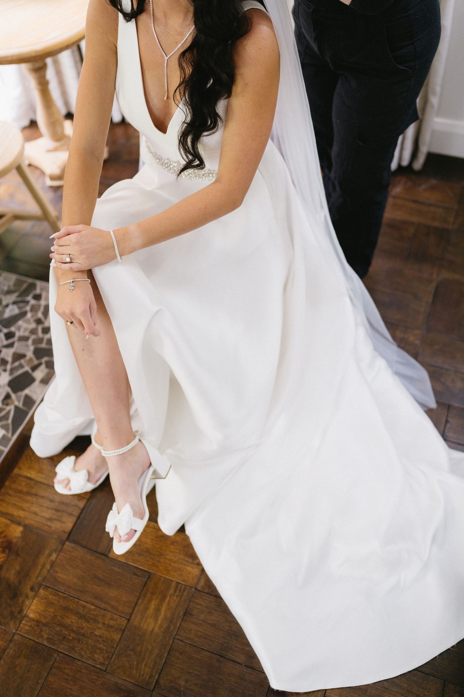 Close-up of bride's feet in white sandals and wedding dress on hardwood floor.