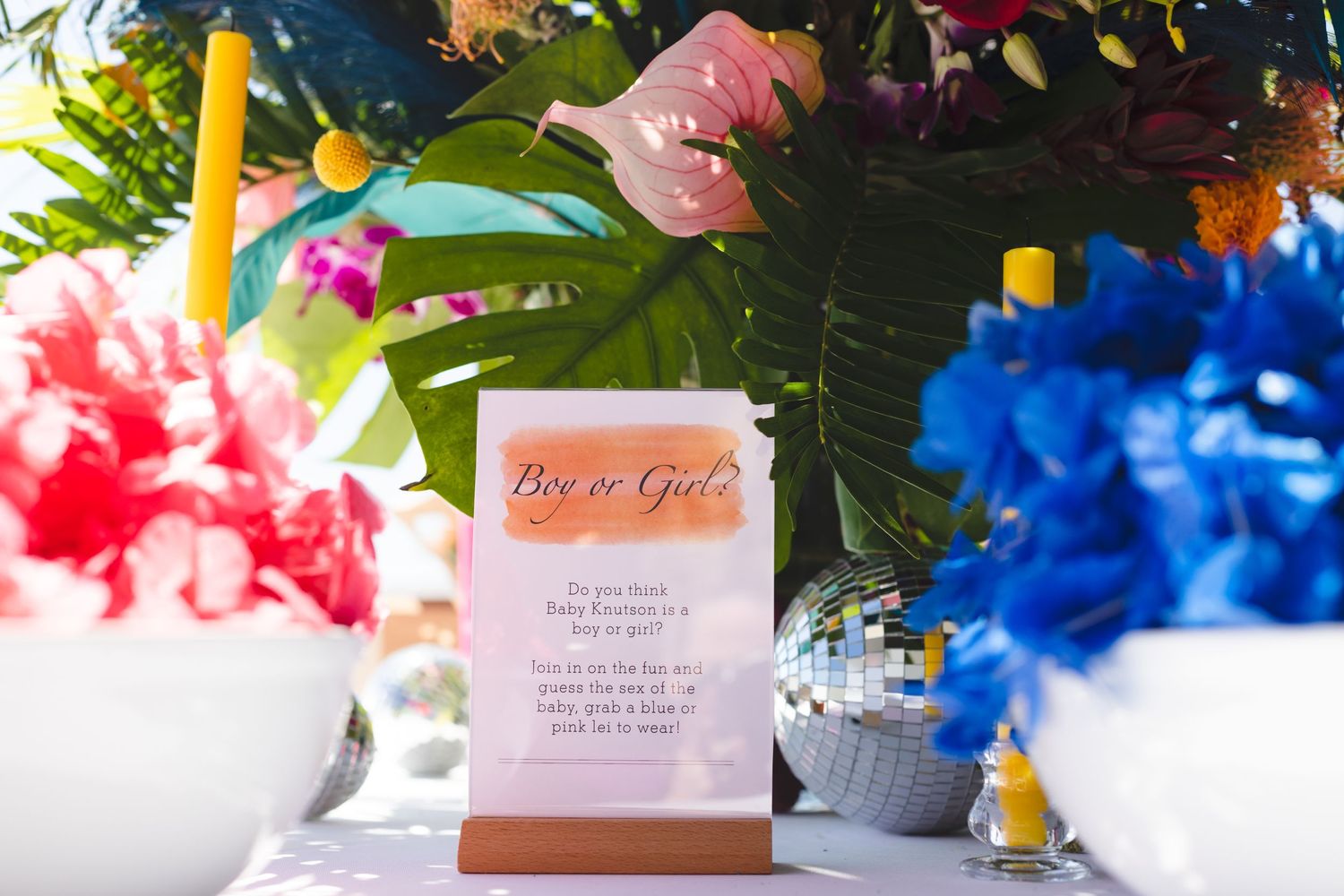 An RSVP card sits among colorful floral decorations with red and blue flowers in a bright party setting.