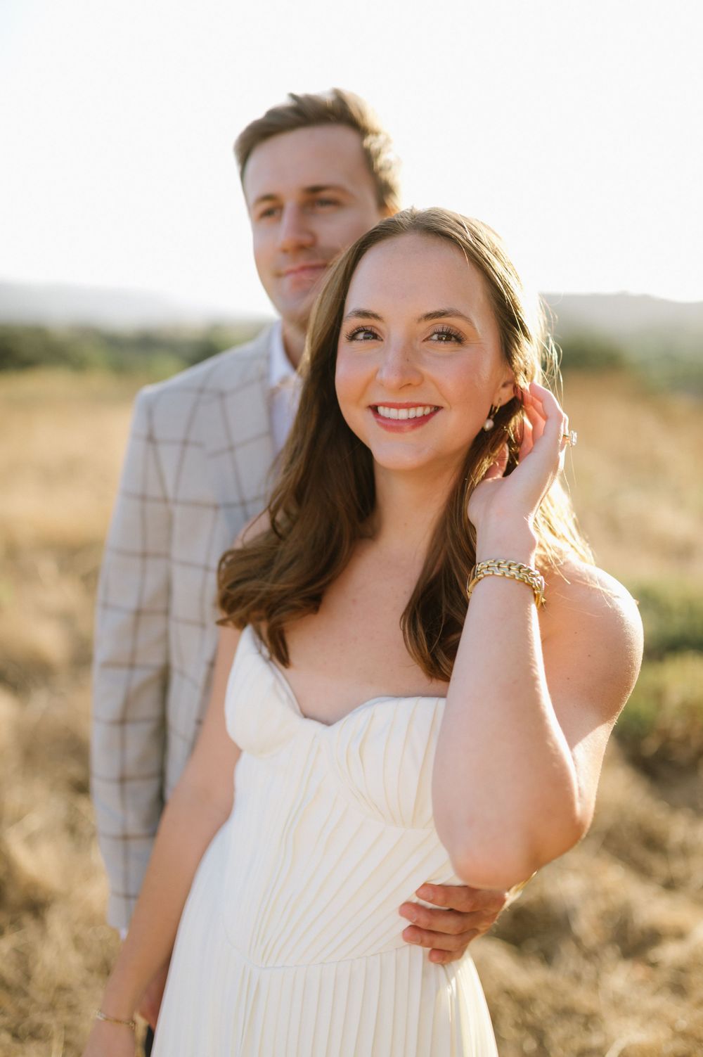 A romantic portrait of a couple posing together in golden sunlight against a rustic countryside background.