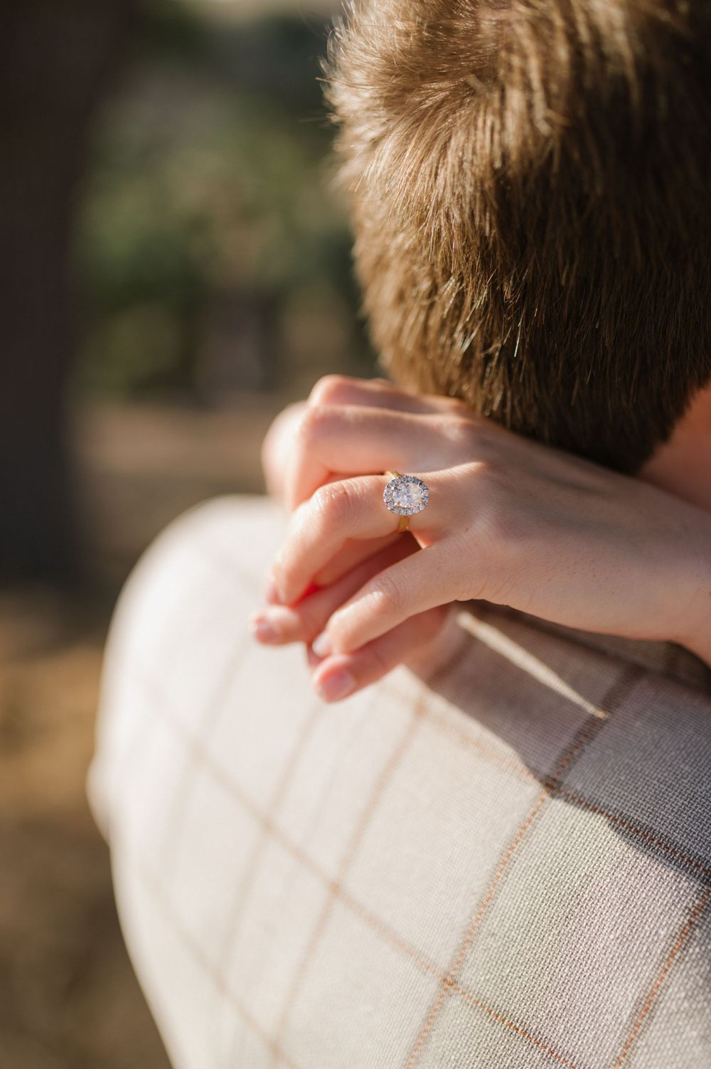 Close-up of hands embracing showing an engagement ring against a checkered jacket.