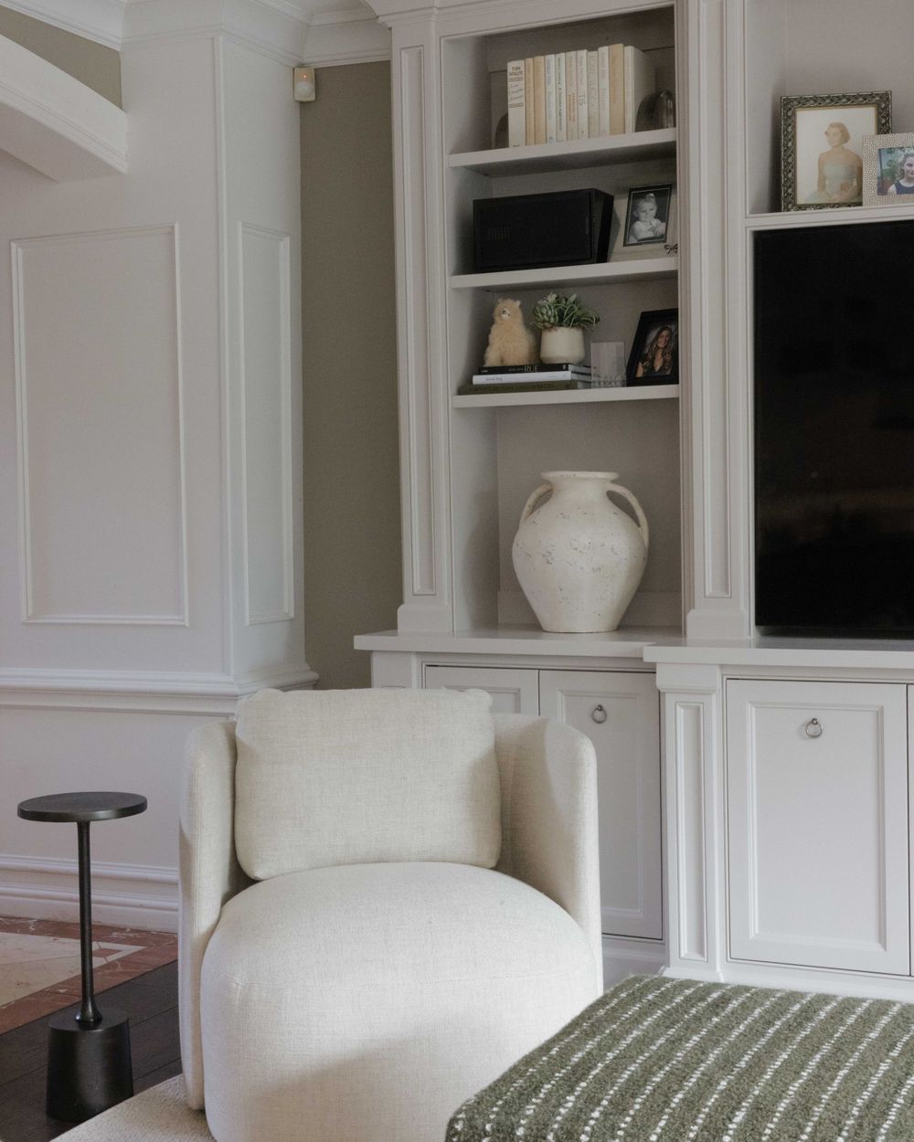 Modern living room corner with curved white armchair, built-in shelves, and decorative white ceramic vase.