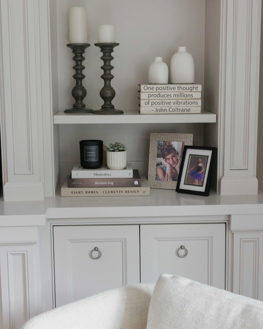 White built-in shelves decorated with candle holders, vases, books, frames and decor in a neutral home interior.