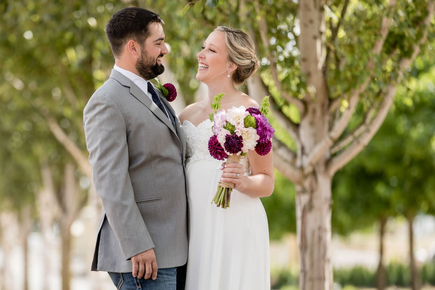 Couple in wedding attire sharing a joyful moment with purple and white bouquet.