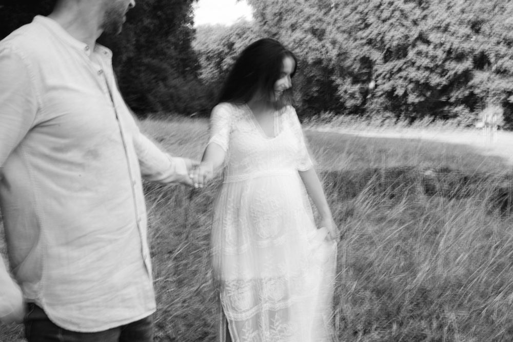 Black and white image of couple in light colored clothing standing in tall grass.