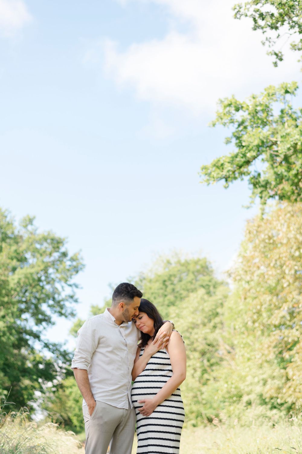 Intimate maternity photo of couple in casual wear standing on nature trail.