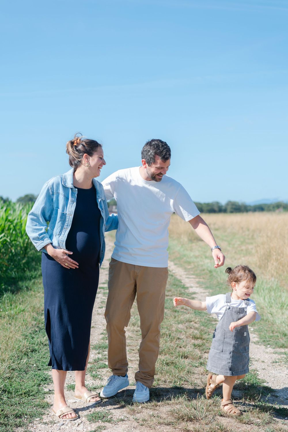 A family enjoying a walk together on a rural path on a sunny day, with a small child running ahead.