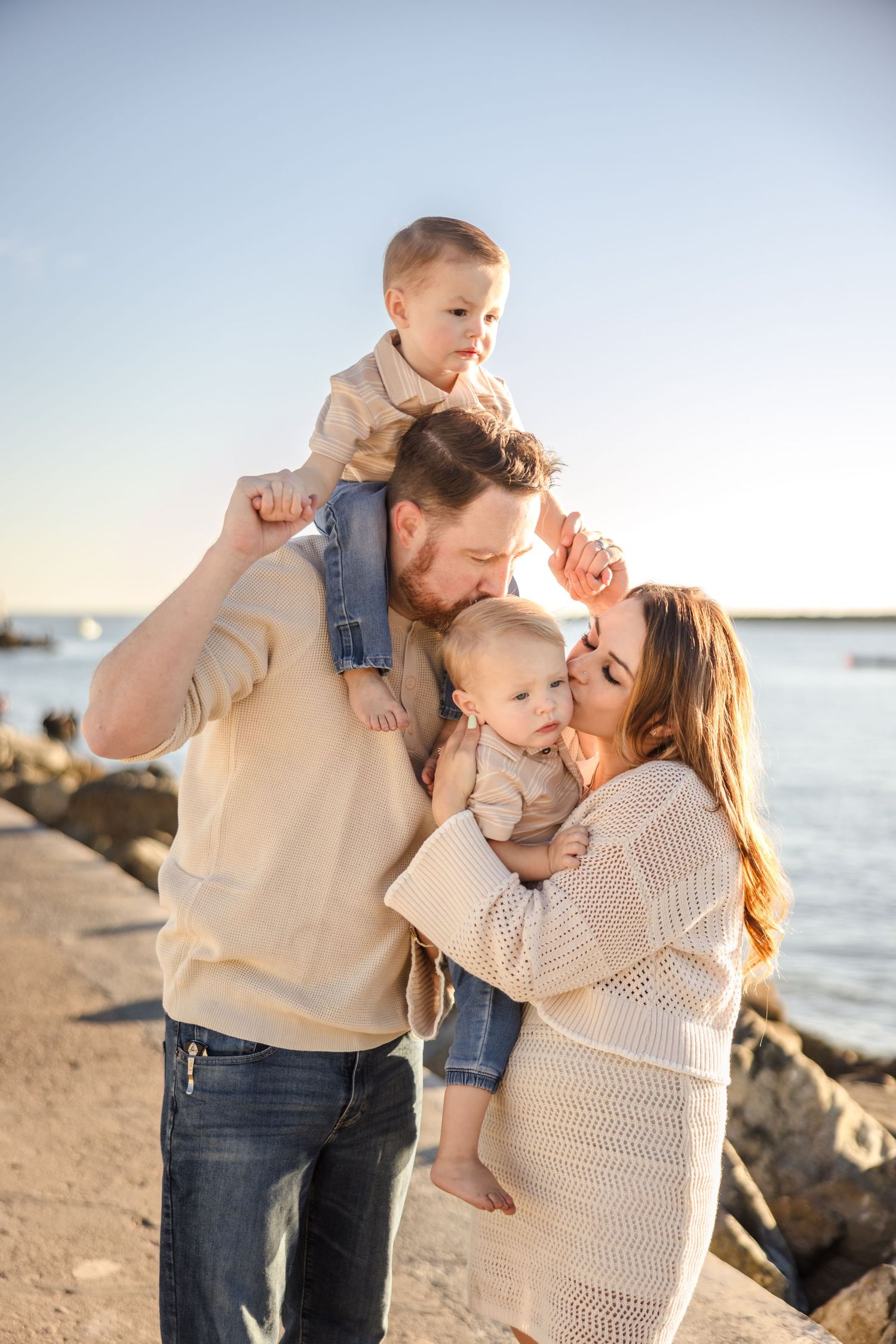 A family shares an intimate moment together by the water during golden hour while standing near rocky shoreline.