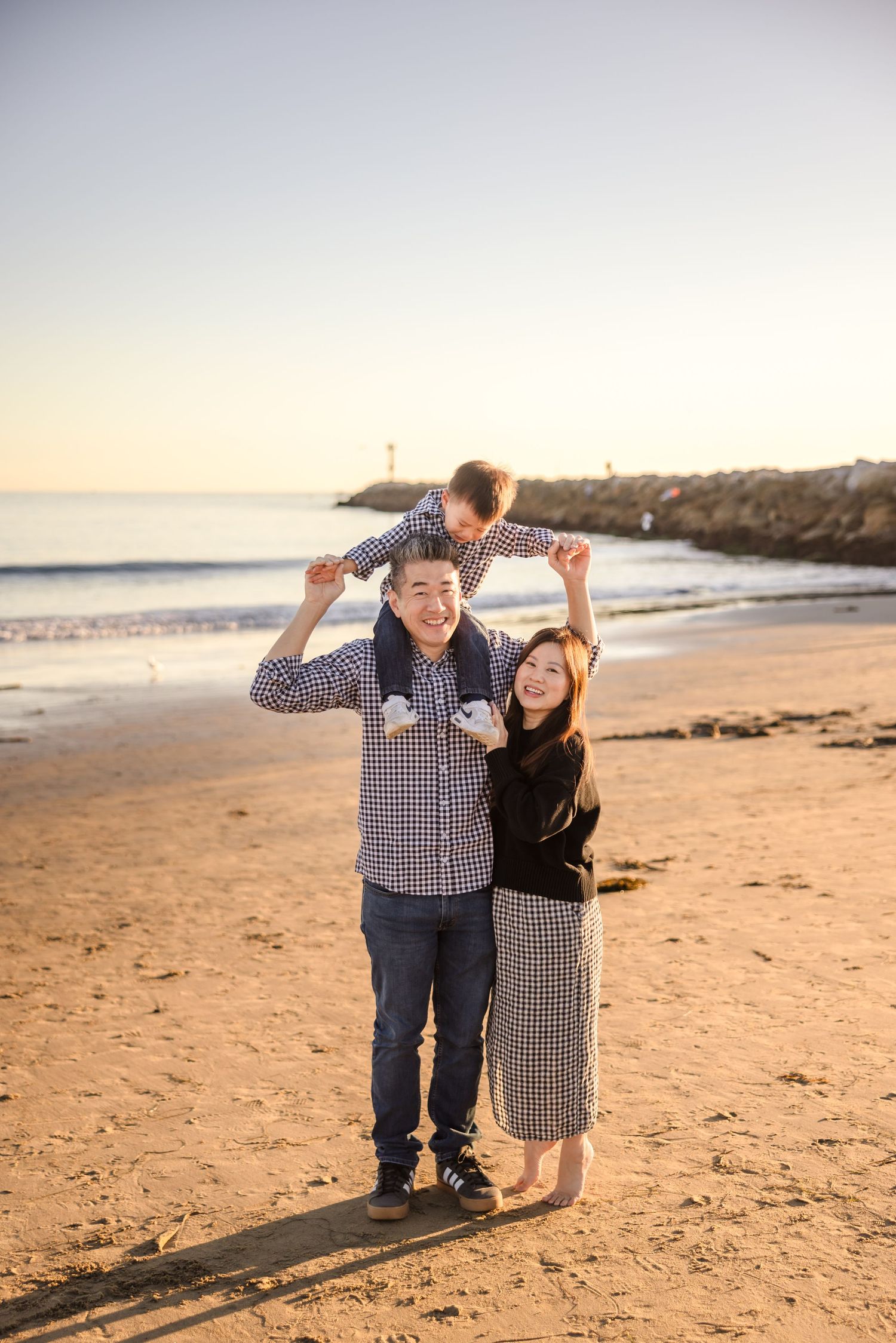 A family enjoying quality time together on a sandy beach at sunset with ocean waves and cliffs in the background.