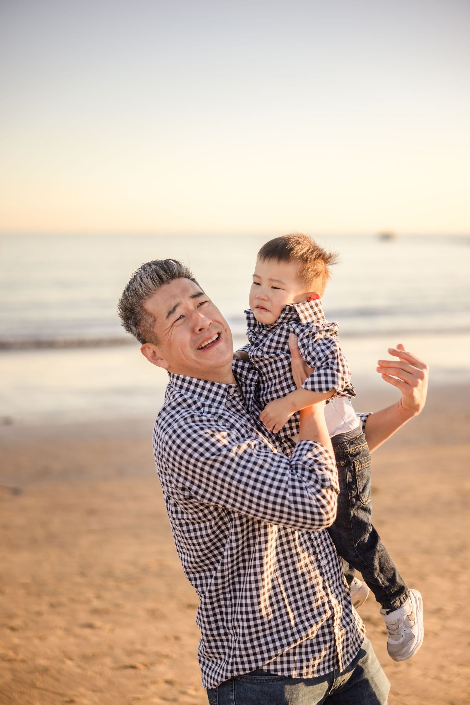 A heartwarming sunset beach scene shows matching blue plaid shirts and joyful laughter during a playful moment on the sand.