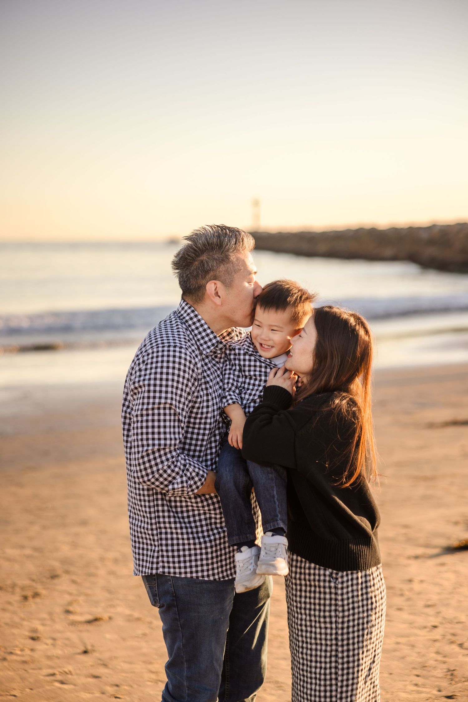 A loving family embraces together on a beach at sunset, with golden light illuminating their tender moment.