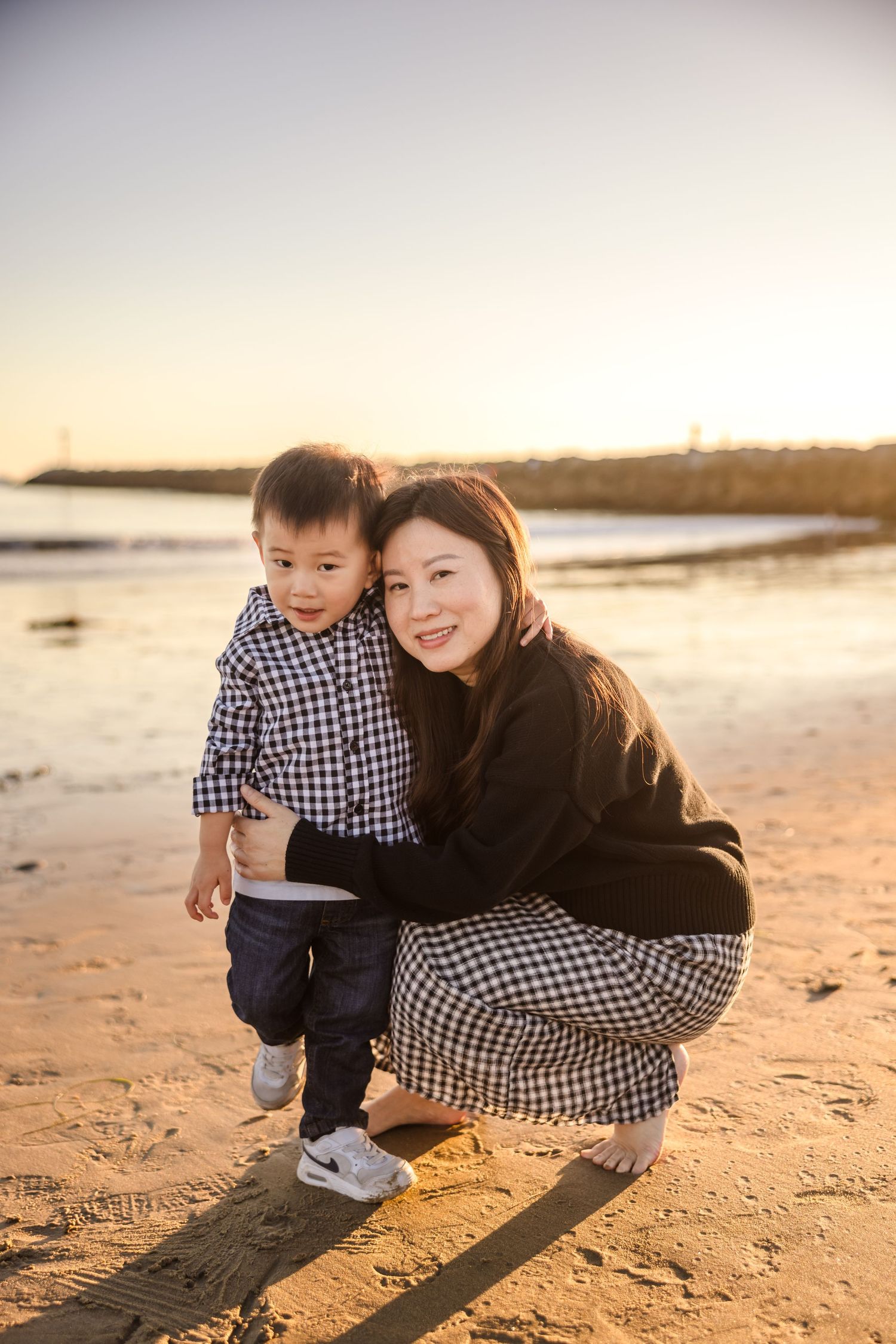 Two people in matching plaid outfits spending time together on a sandy beach during golden hour sunset.