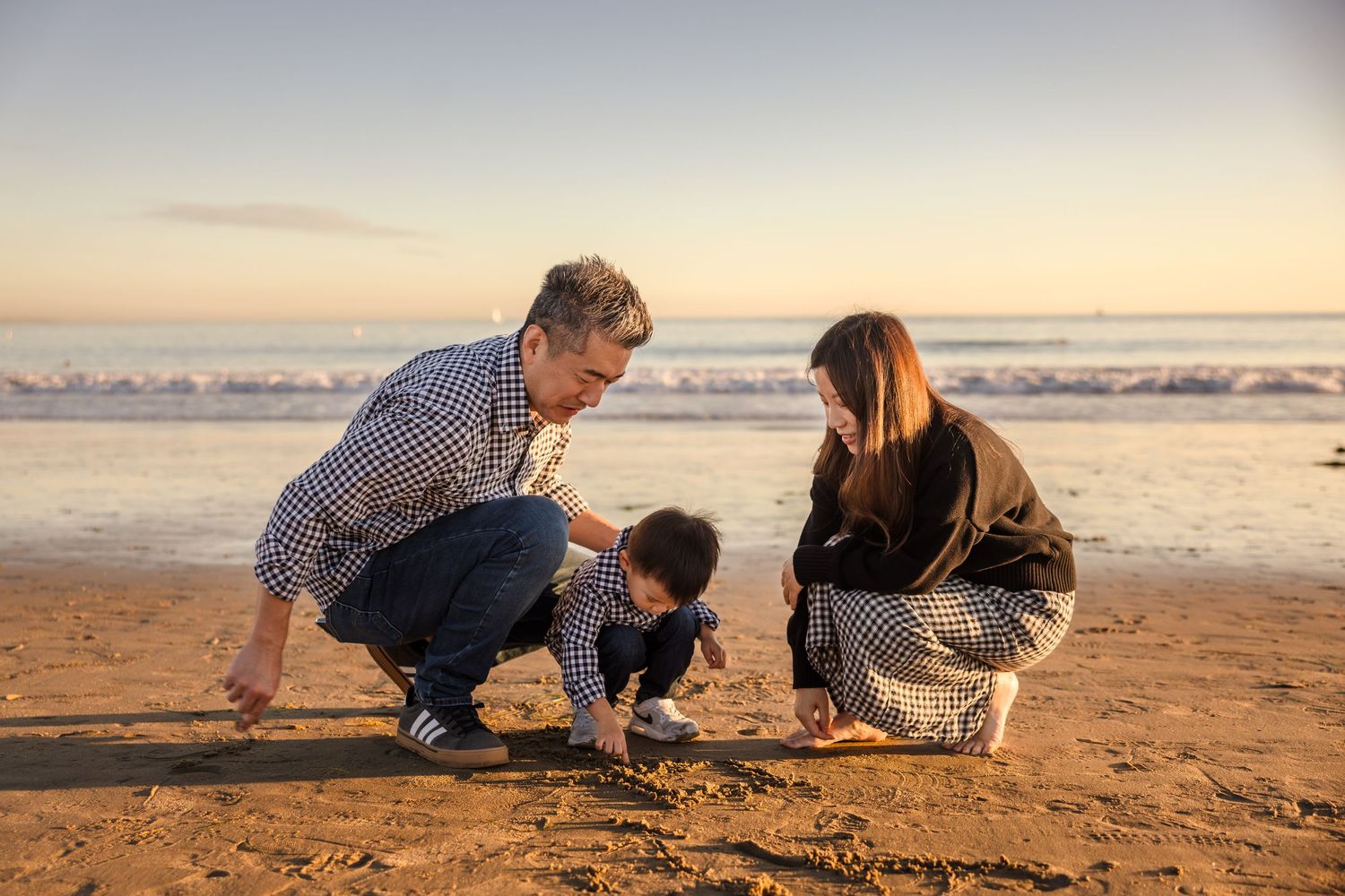 Three people crouching together on a sandy beach during sunset exploring the shoreline.