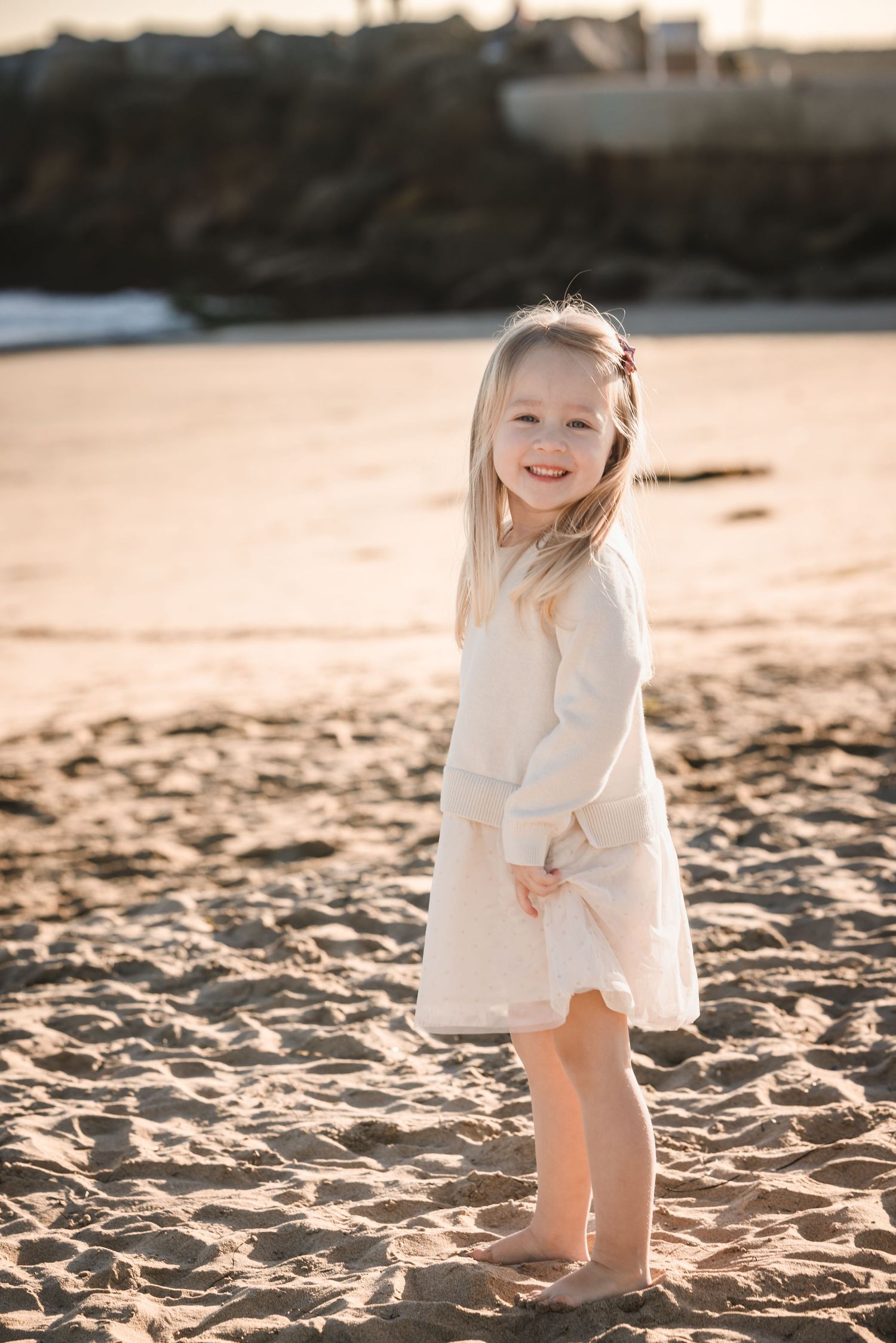 Young child in a white dress playing on a sunny beach during golden hour.