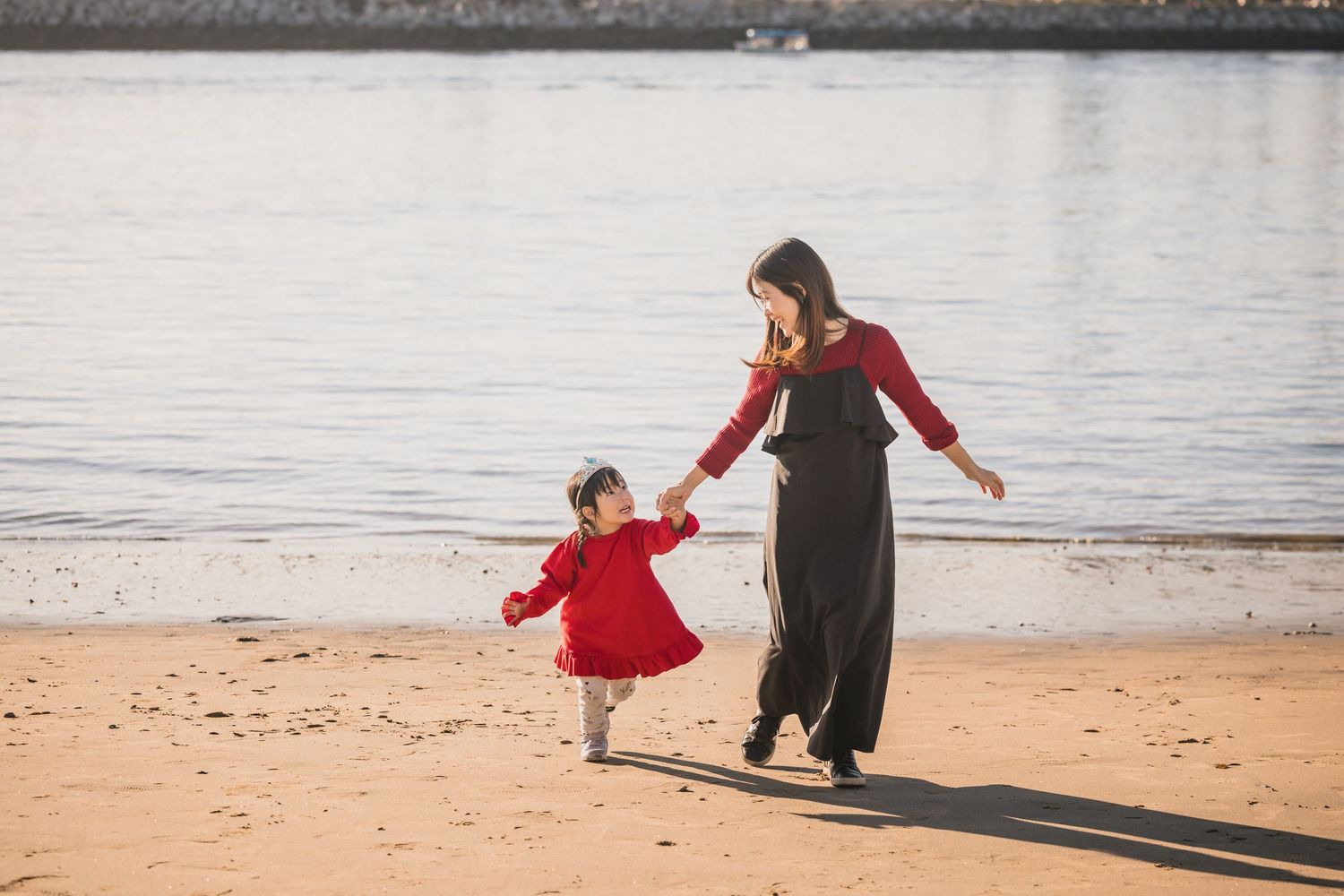 Two figures in coordinating red and black outfits dance together on a sandy beach at sunset by the water.