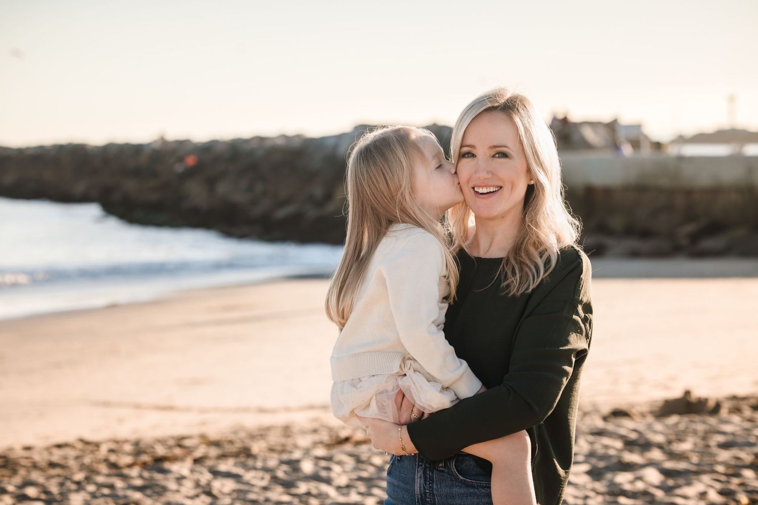 A tender beach moment captured at sunset with warm lighting and coastal scenery in the background.