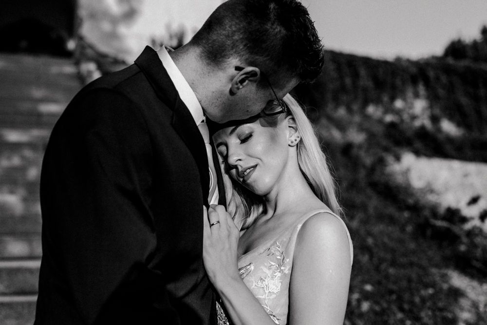 A black and white intimate wedding portrait showing a tender moment between newlyweds outdoors.