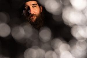 Dramatic side profile portrait of a bearded person against a dark background with bokeh lights.