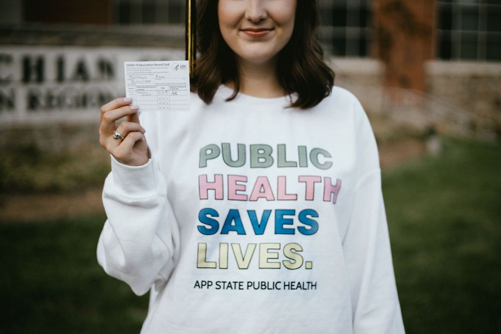 Person wearing white sweatshirt with Public Health Saves Lives text printed in pastel colors.