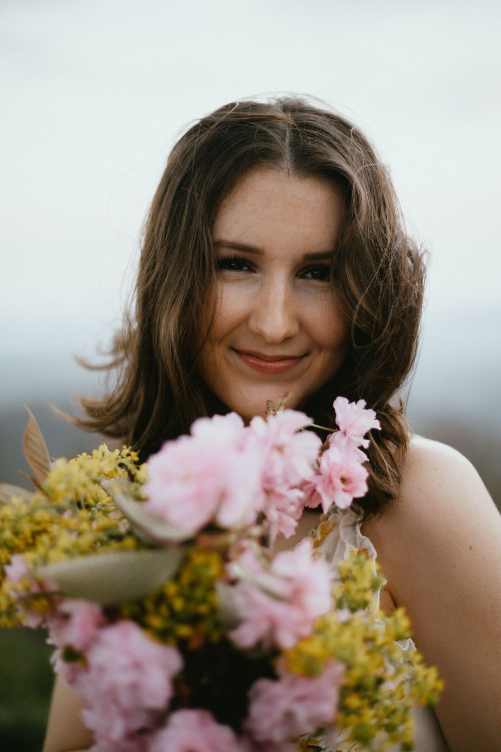 Portrait with pink and yellow flowers in soft natural lighting outdoors.