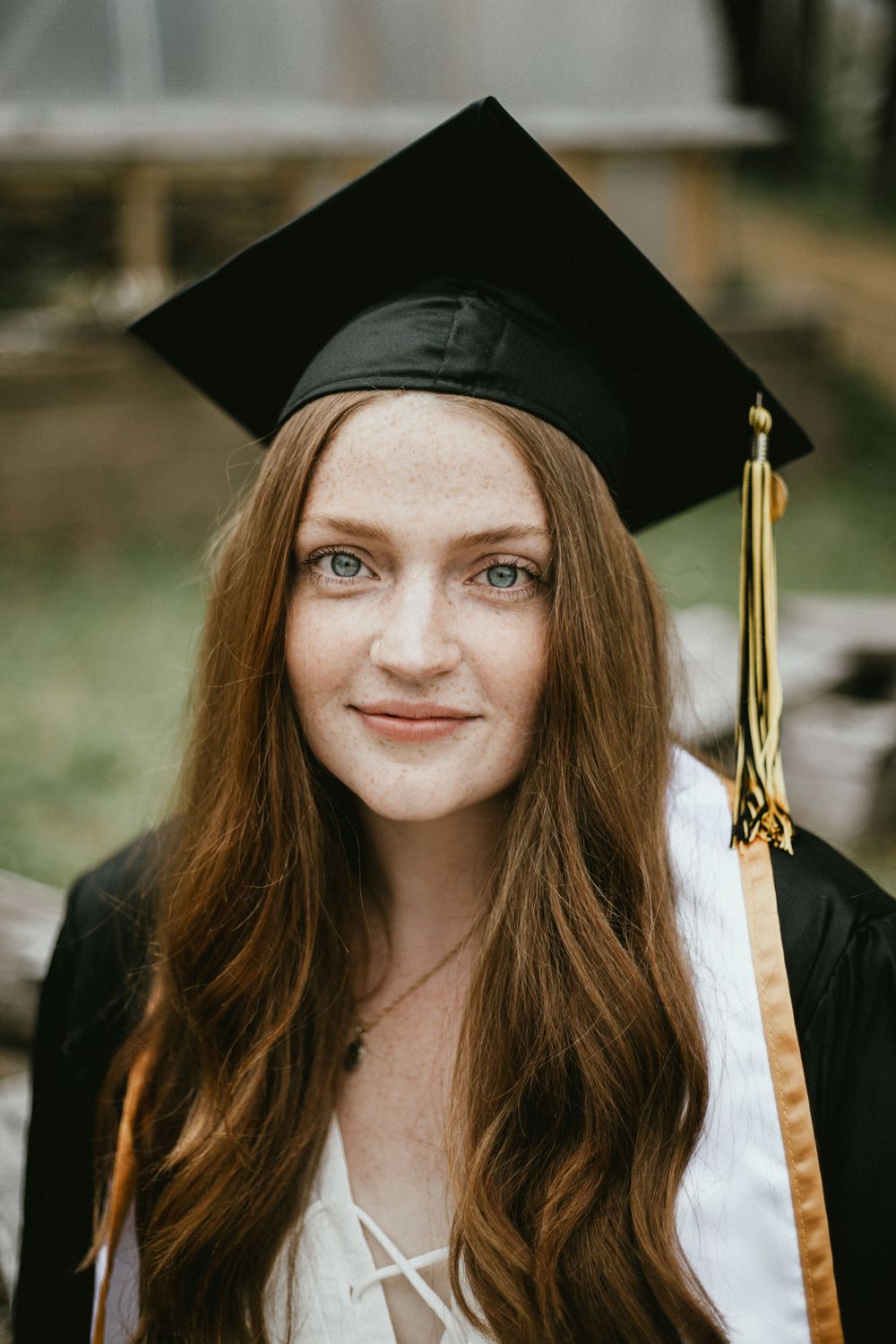 Graduate wearing traditional black cap with gold tassel poses against natural outdoor background.