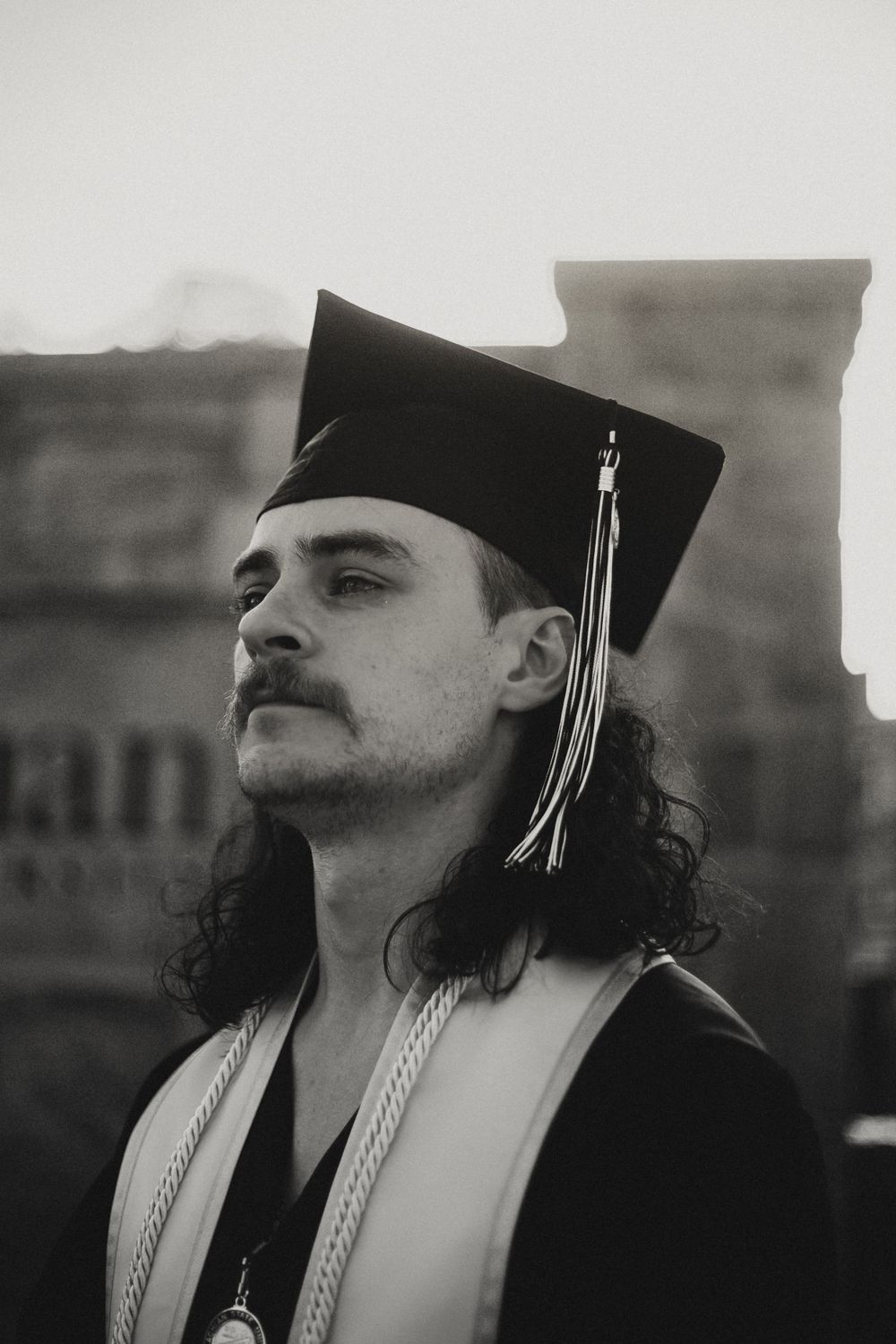 Black and white portrait of graduate in cap and gown with vintage film aesthetic.