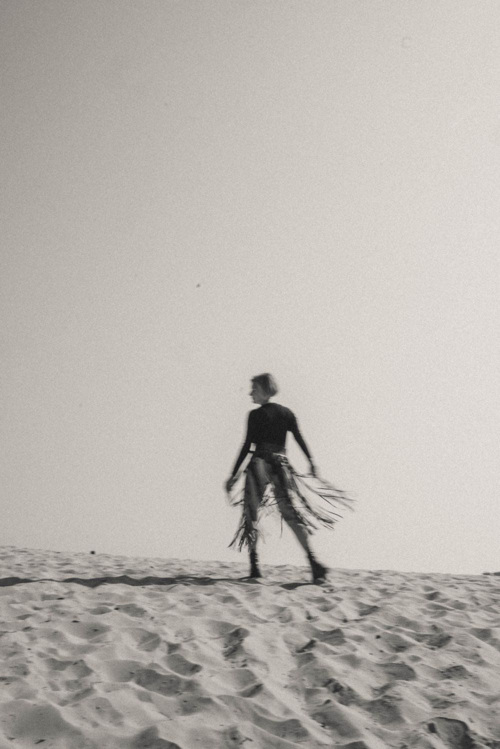 Silhouette of person standing on beach with flowing fabric in black and white.