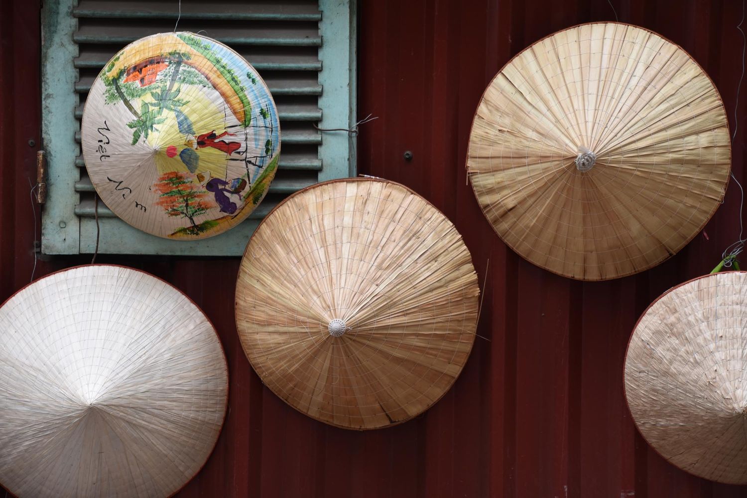 Traditional Asian paper parasols in white and tan colors displayed against a red wall with shutters.