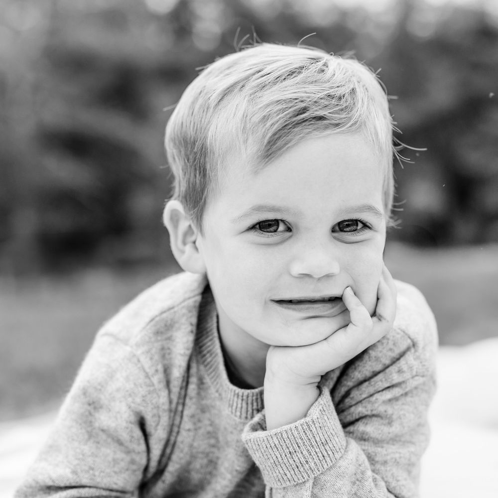 Black and white portrait of young child resting chin on hand with gentle smile.