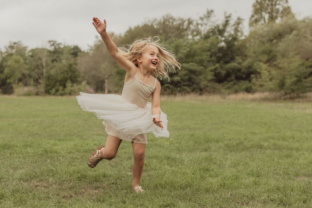 Young dancer in tulle dress leaps joyfully across green field.