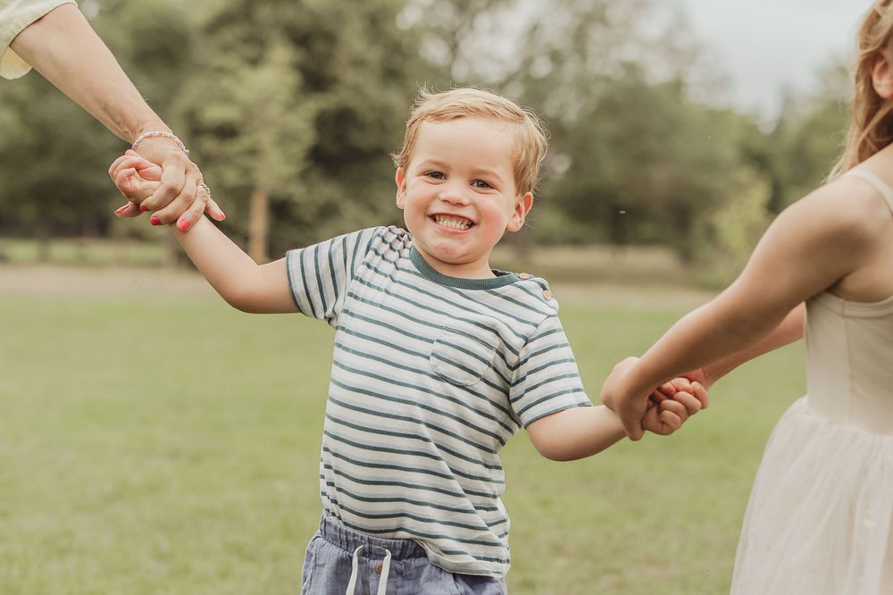 A child in a striped shirt plays outdoors in a grassy field on a sunny day.