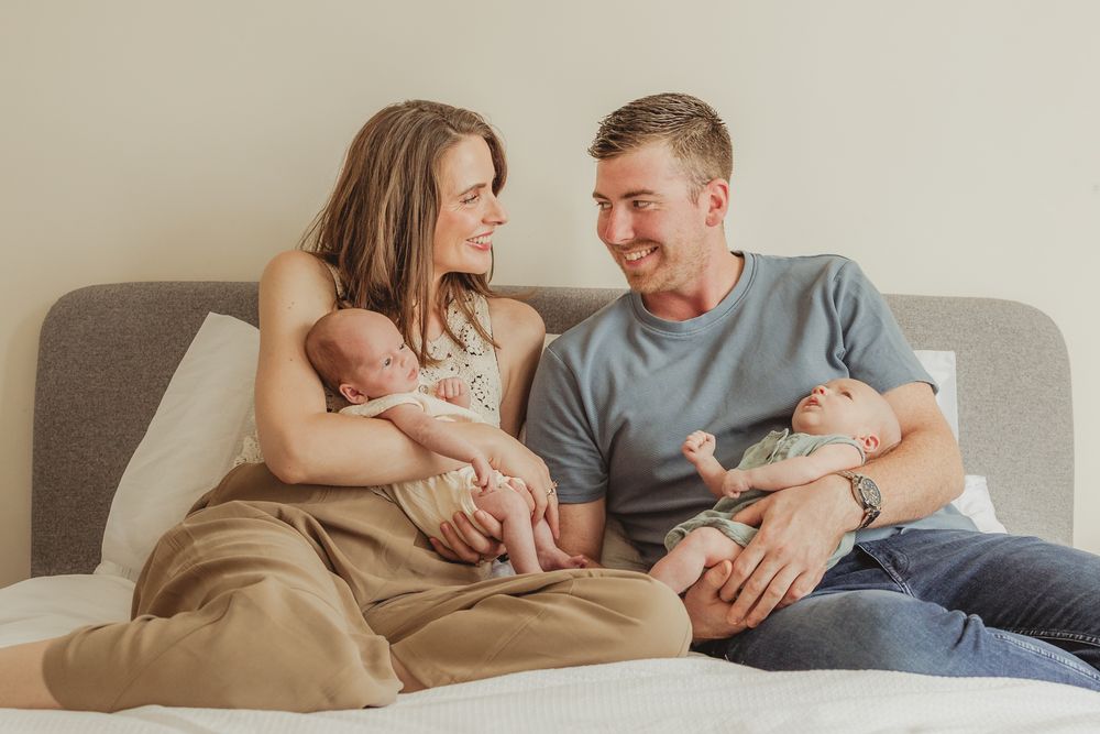 Family relaxing together on grey bed with newborn baby.