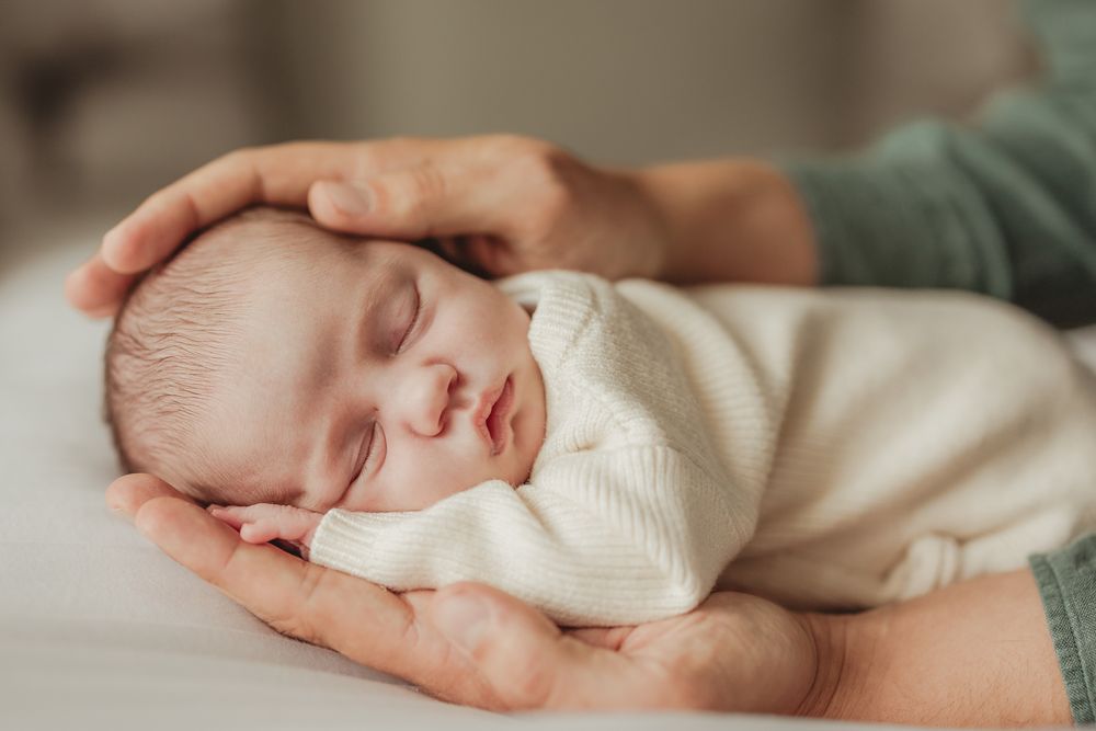 Sleeping newborn baby wrapped in white blanket rests peacefully on soft bedding.