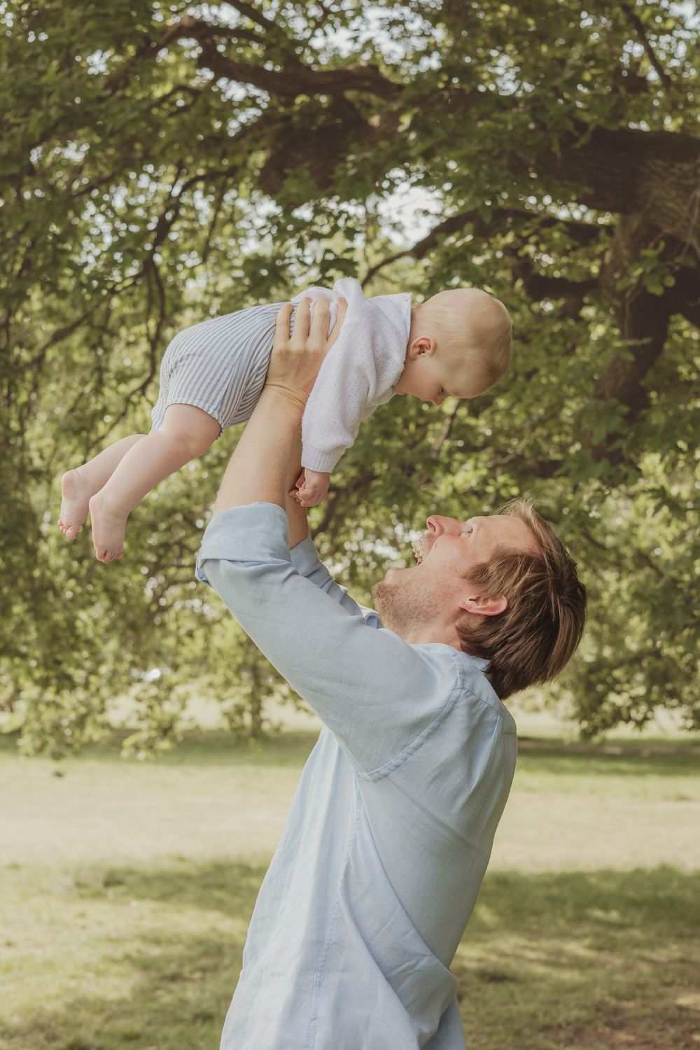 An outdoor photo of a father (dad) throwing his baby in the air and catching him