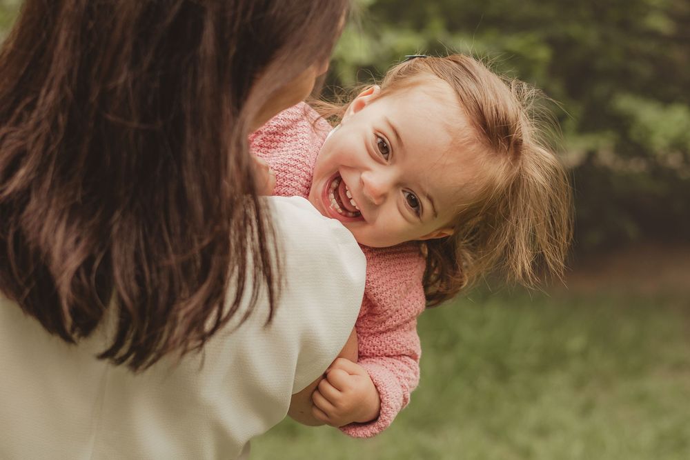 toddler in pink jumper laughing over mum's shoulder