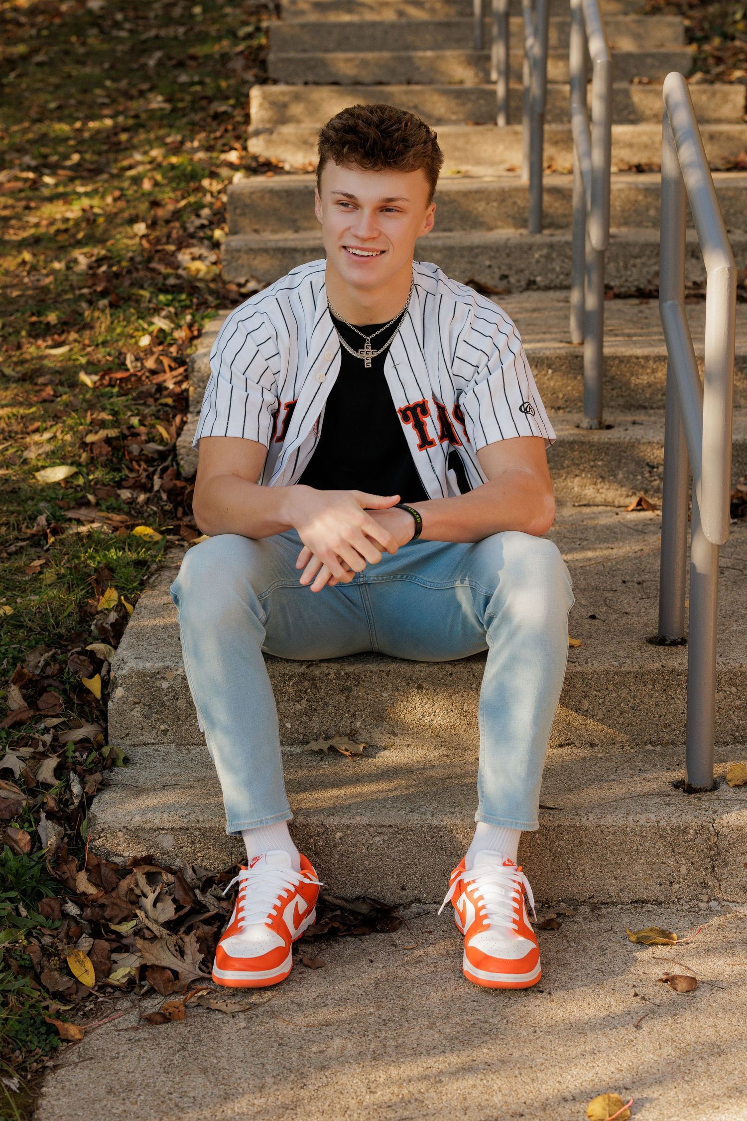 Someone in a pinstriped baseball jersey and light jeans sits casually on outdoor concrete steps wearing orange and white sneakers.