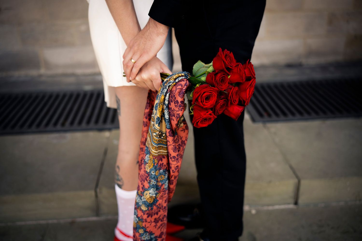Romantic close-up of a couple holding hands, with red roses and vintage fashion—capturing love, style, and heartfelt moments.