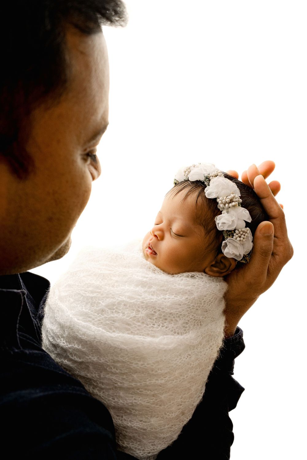 Newborn baby sleeping on fathers hand with white floral headband wrapped in white lace wrap